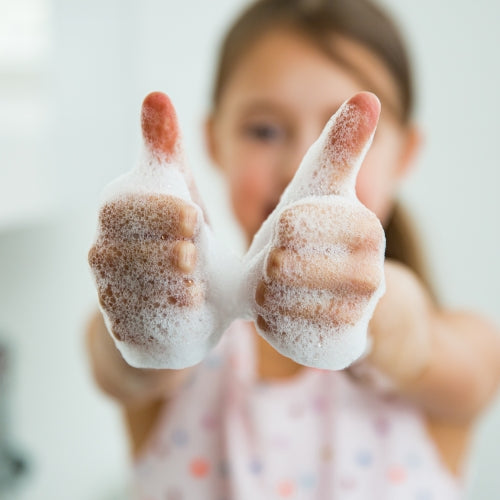 Ein Kind, dass die Daumen hochstreckt und Schaum an den Händen hat.