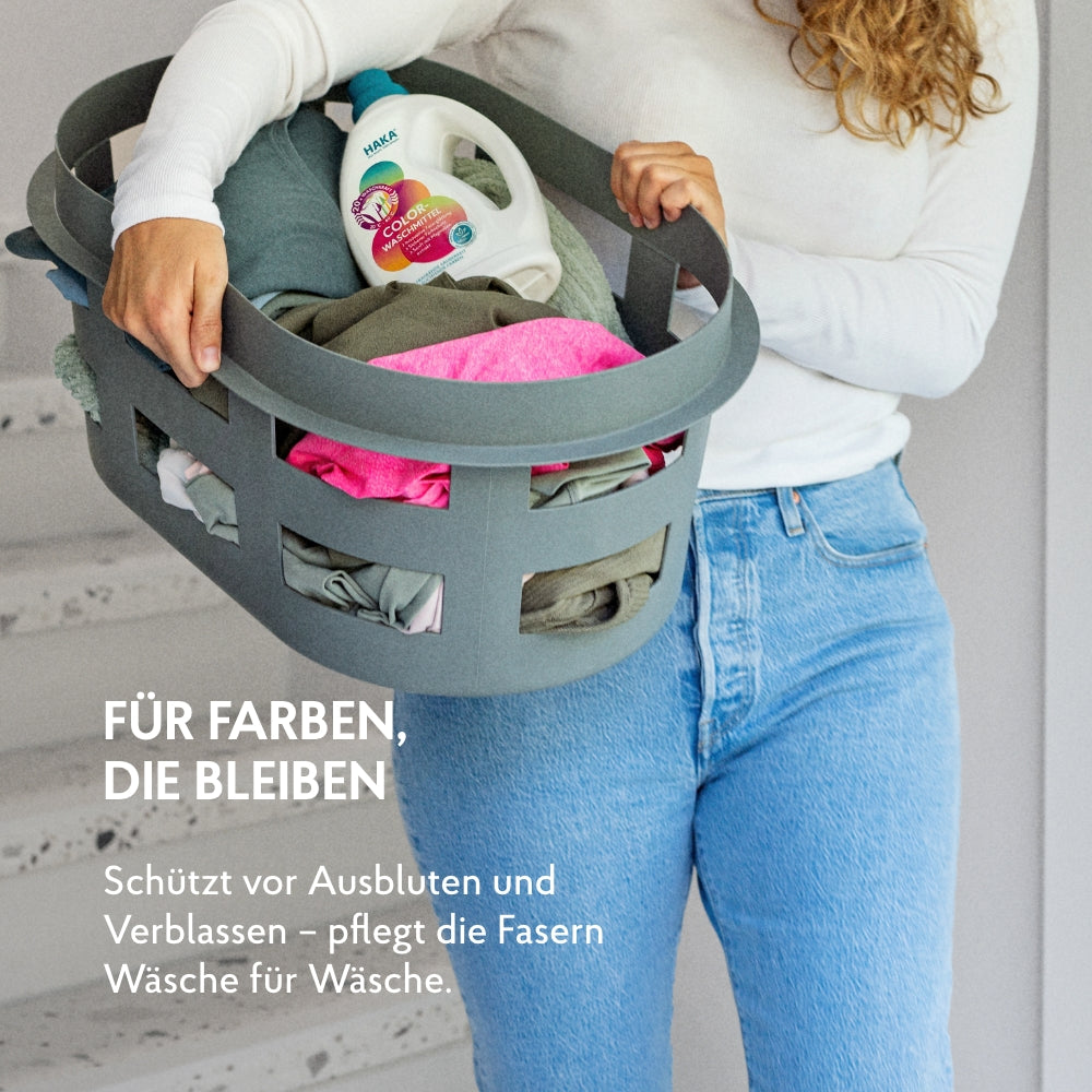 Frau mit Wäschekorb der mit bunter Kleidung und dem Colorwaschmittel bestückt ist