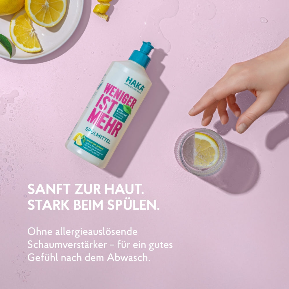 Spülmittel 475ml Flasche liegt auf dem Tisch und eine Hand greift nach einem gefülltem Wasserglas mit Zitronenscheibe